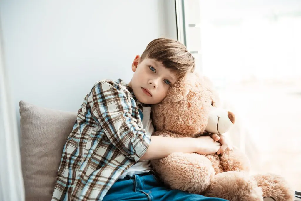 little boy hugging a teddy bear while looking at us, symbolizing his future as he suffers from childhood trauma and addiction