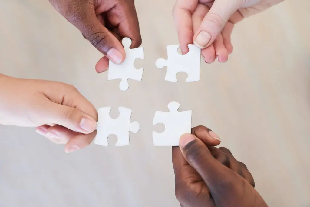 four hands holding puzzle pieces, showing we need unity to break the stigma of addiction