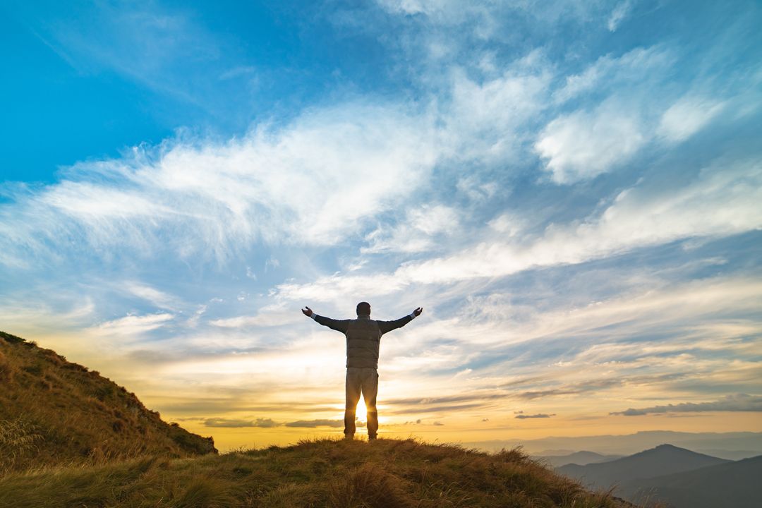 man on mountain embracing the sunrise with outstretched arms