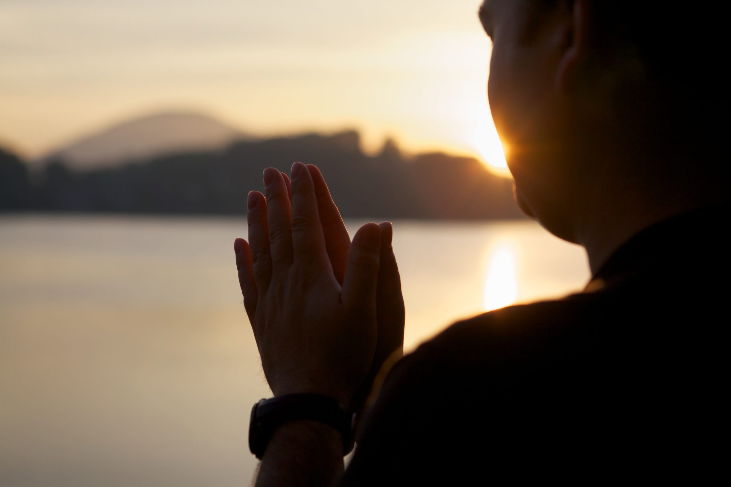 a man praying with the sunset and lake in the background, highlighting the effectiveness of religion and addiction recovery